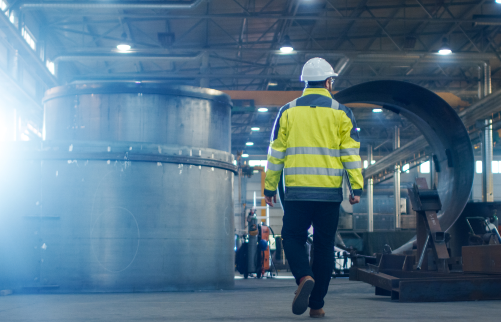 Picture of a worker in high vis and a hard hat walking through an industrial factory.