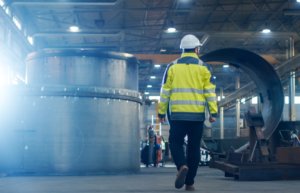 Picture of a worker in high vis and a hard hat walking through an industrial factory.