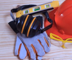 Picture of a trades person's hat, gloves, level and ear protectors.